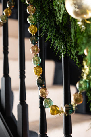 The Black, Green & Gold Bauble Garland styled on a styled stairs with greenery and gold bauble