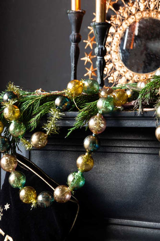 The Black, Green & Gold Bauble Garland hung over the edge of a black fireplace styled with a conifer branch garland.