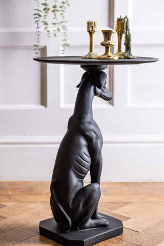 The Black Greyhound Dog Side Table seen from the back, styled with three gold candlesticks on top.