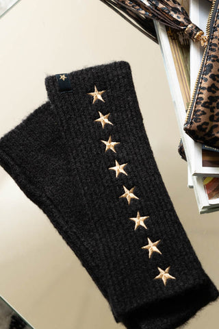 The Black Handwarmers With Gold Stars displayed on a table with some magazines and a leopard print bag.