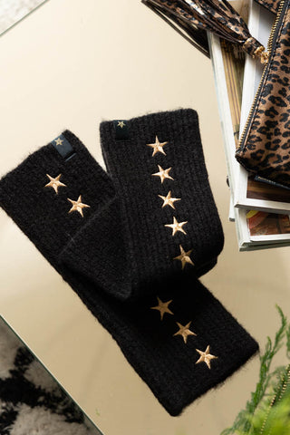 The Black Handwarmers With Gold Stars displayed on a surface with some magazines, a plant and a leopard print bag.