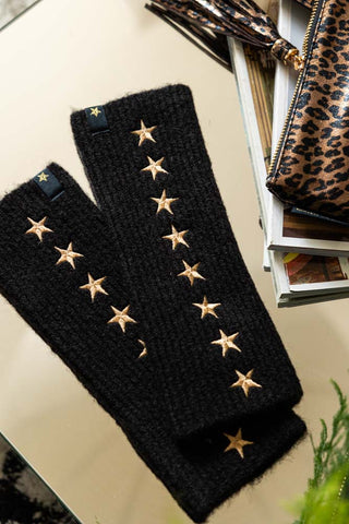 The Black Handwarmers With Gold Stars displayed on a surface with some magazines, a plant and a leopard print bag.