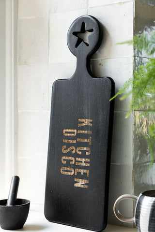 The Black Kitchen Disco Slim Serving Board leaning against a tiled wall in a kitchen.