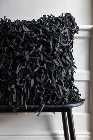 The Black Leather Cushion Cover displayed on a black bench in front of a white wall.