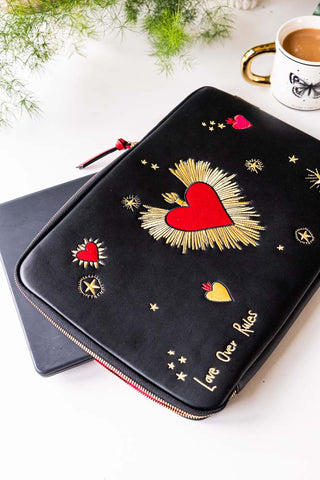 The Black Milagro Heart Laptop Case styled on a table with a laptop, mug, mug and plant.