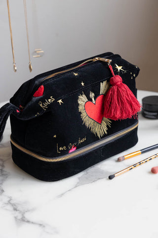 The Black Milagro Heart Velvet Wash Bag styled on a white table with makeup brushes and jewellery.