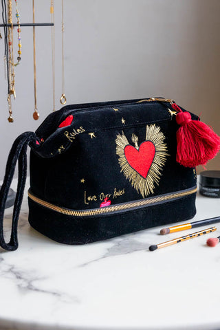 The Black Milagro Heart Velvet Wash Bag displayed on a white table with some makeup, brushes and a jewellery stand.