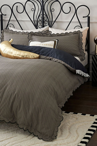 The Black Pencil Stripe Scalloped Edge Bedding Set styled on a bed with cushions.