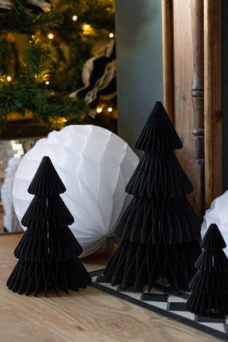 The Set Of 3 Black Honeycomb Christmas Trees styled next to white paper decorations in front of a christmas tree.