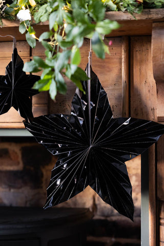 The Set Of 3 Black Gloss Paper Stars hung under a wooden mantlepiece with a green leaf garland above.