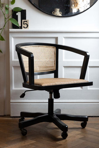 A wicker desk chair on a wooden floor, in front of a white wall with a large mirror and number decorations.