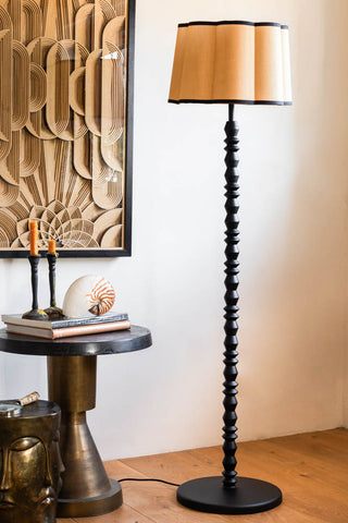 The Black Wood Spindle Floor Lamp - Base Only, displayed with a shade on next to a side table styled with various accessories.