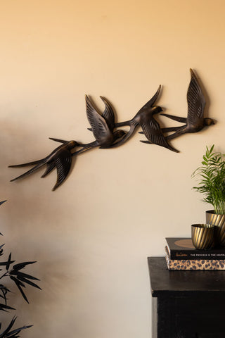 The Antiqued Brass Effect Bird Wall Art displayed on a neutral wall, above a sideboard with books and plants.