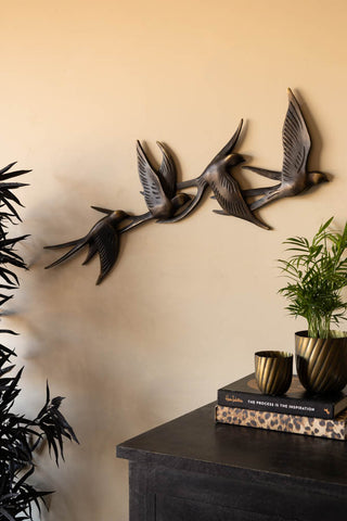 The Antiqued Brass Effect Bird Wall Art styled on a neutral wall, with plants, books and a wooden sideboard.