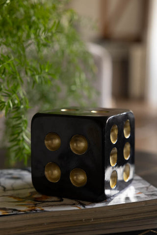 The Black & Gold Dice Ornament styled on a table on top of some magazines, with greenery in the background.