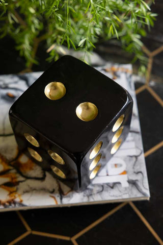 The Black & Gold Dice Ornament seen from above, styled on a table on some magazines, next to a plant.