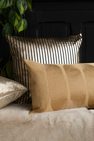 The Black & Gold Striped Cushion styled with two others on a faux fur throw, with some greenery.