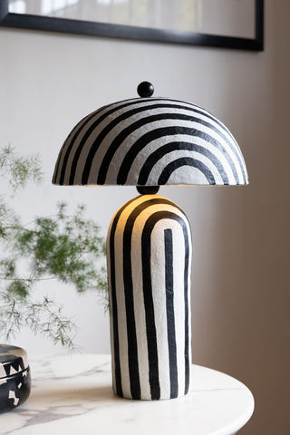 The Black & White Stripe Paper Mache Table Lamp displayed on a white table.