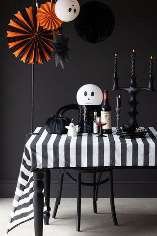 The Black & White Striped Tablecloth styled on a tablescape in a black room with various decorations and tableware.