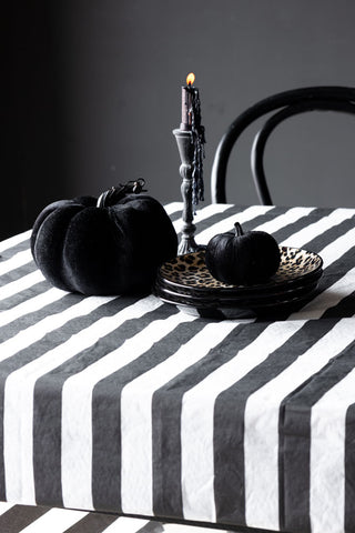 The Black & White Striped Tablecloth styled with plates, black pumpkins and a candlestick holder with melted wax dripping from the lit candle.