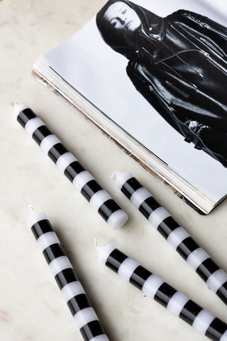 The Black & White Striped Taper Candles - Pack Of 4 styled on a light surface with a book.