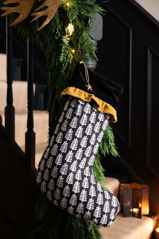 The Luxury Christmas Tree Stocking hanging from some stairs with garlands, with some candles on the stairs in the background.