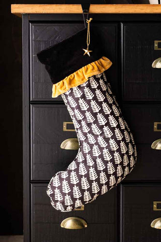 The Block Print Christmas Stocking hanging in front of a black and wooden storage unit.