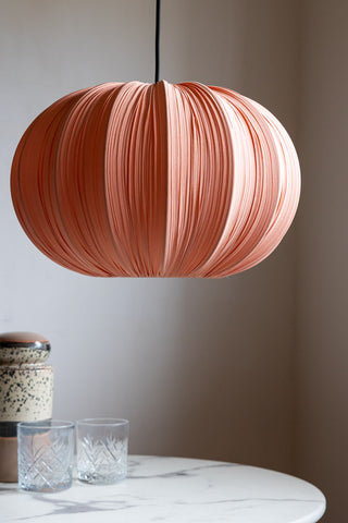 The Blush Pleated Fabric Ceiling Light hanging in front of a neutral wall above a marble table, styled with some glasses and a storage jar.