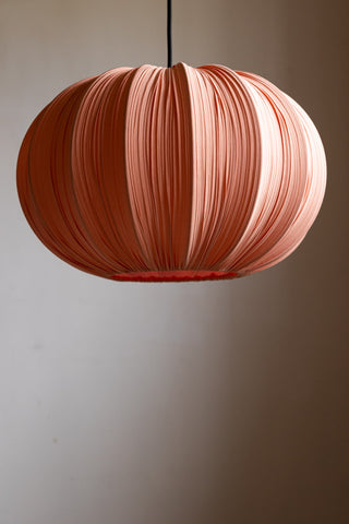 The Blush Pleated Fabric Ceiling Light hanging in front of a neutral wall.