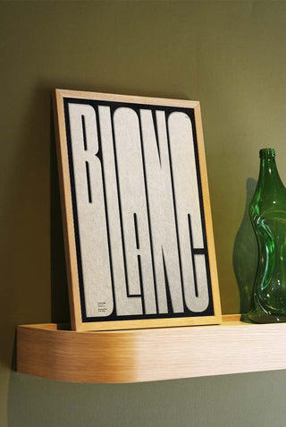 The Bold Blanc Art Print styled in a frame, displayed leaning against a wall on a shelf.