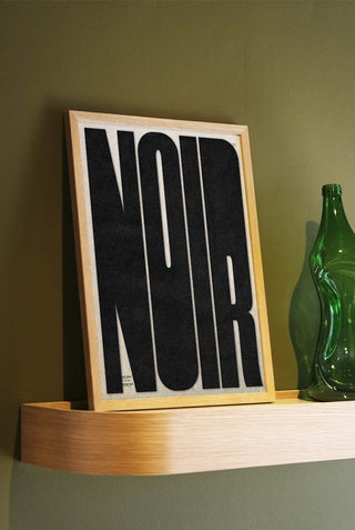 The Bold Noir Art Print styled in a frame on a shelf, leaning against the wall.