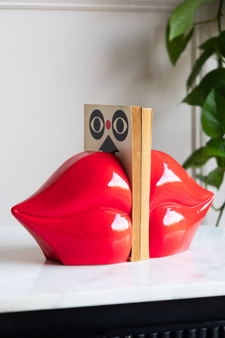 Bright and bold red lips bookends with two books between the bookends on a black and white console table.