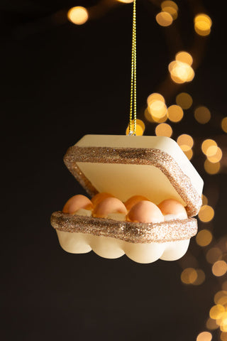 The Box Of Eggs Christmas Tree Decoration hanging in front of a dark background with fairy lights.