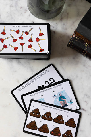 Some of the cards from the Brain Training While You Poo Card Pack displayed on a white marble table with some books and a soap dispenser.