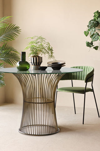 The Bronze & Glass Round Dining Table styled with various dining accessories on, with a green dining chair and several plants.