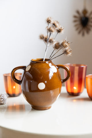 The Brown & Ivory Dotted Display Vase with flowers inside, styled on a table with lit tealights in tealight holders and a small ornament.