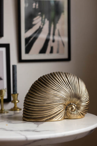 Lifestyle shot of the Brushed Gold Faux Sea Shell Ornament, styled with candlestick holders and art prints.