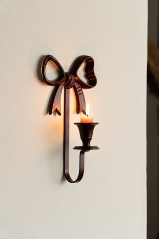 The Burgundy Red Bow Wall-Mounted Candle Holder on a neutral wall with a lit candle inside.