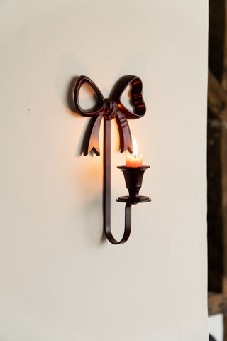 The Burgundy Red Bow Wall-Mounted Candle Holder on the wall, with a lit candle inside.