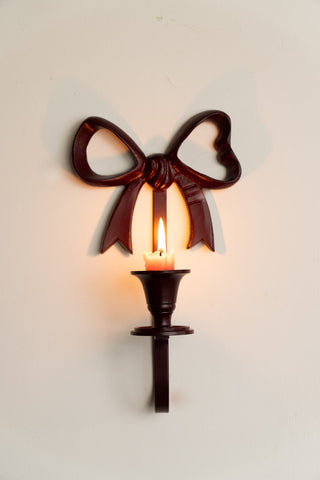 The Burgundy Red Bow Wall-Mounted Candle Holder displayed on a neutral wall, with a lit candle inside.