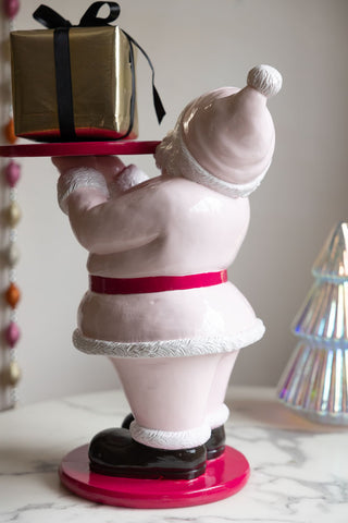 The Butler Santa In Pink Christmas Decoration seen from the back, styled with a present on, next to a Christmas tree ornament and a garland.