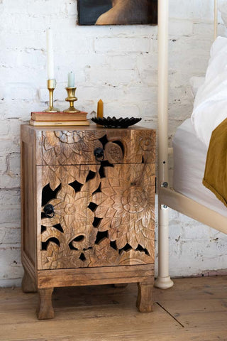 The Carved Floral Design Wood Bedside Table styled next to a bed with candlesticks and home accessories.