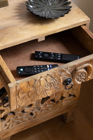 The Carved Floral Design Wood Bedside Table with the drawer open and some remote controllers inside.