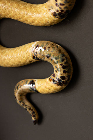 Close-up of the tail of the Ceramic Snake Wall Art, displayed on a black wall.