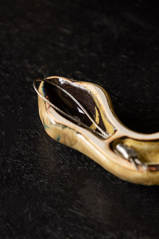 Close-up of the reverse side of the snake's head on the Ceramic Snake Wall Art, displayed on a dark wooden surface.