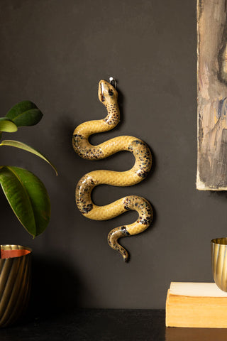 A ceramic snake displayed on the wall surrounded by other home accessories and a plant.