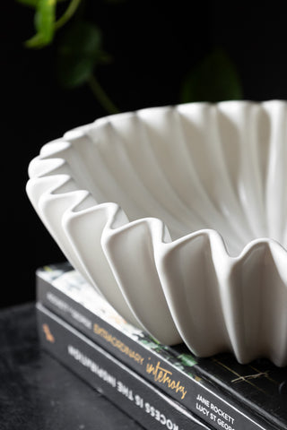 Close-up of the White Ceramic Waved Bowl styled on a stack of books on a black surface.