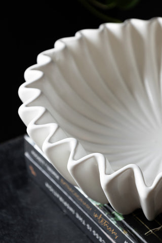 Detail shot of the White Ceramic Waved Bowl styled on a stack of books on a black surface, seen from above.