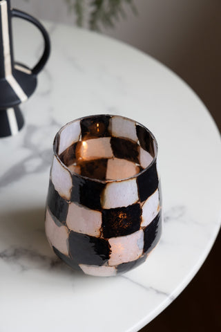 The Checkered Black & White Glass Tealight Holder seen from above, styled on a round marble table with a vase and plant in the background.