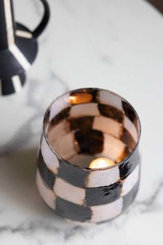 The Checkered Black & White Glass Tealight Holder seen from above, displayed on a table with a lit tealight inside, next to a vase.